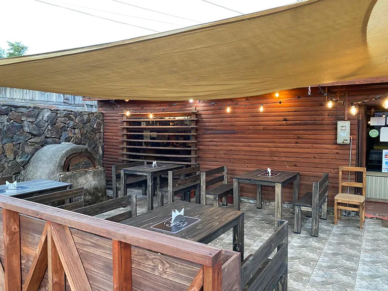 Terraza con mesas y bancas de madera bajo un toldo
